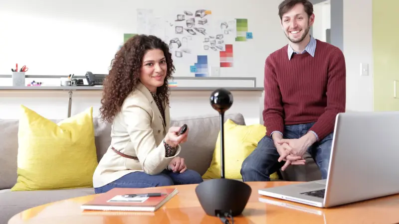 Logitech BCC950 webcam and speakerphone on a table with two people in a modern office setting.